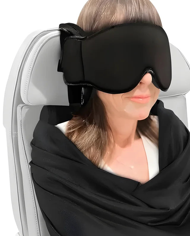 A traveler in a seat wearing the eye mask on the head pillow, with the body sling draped over her